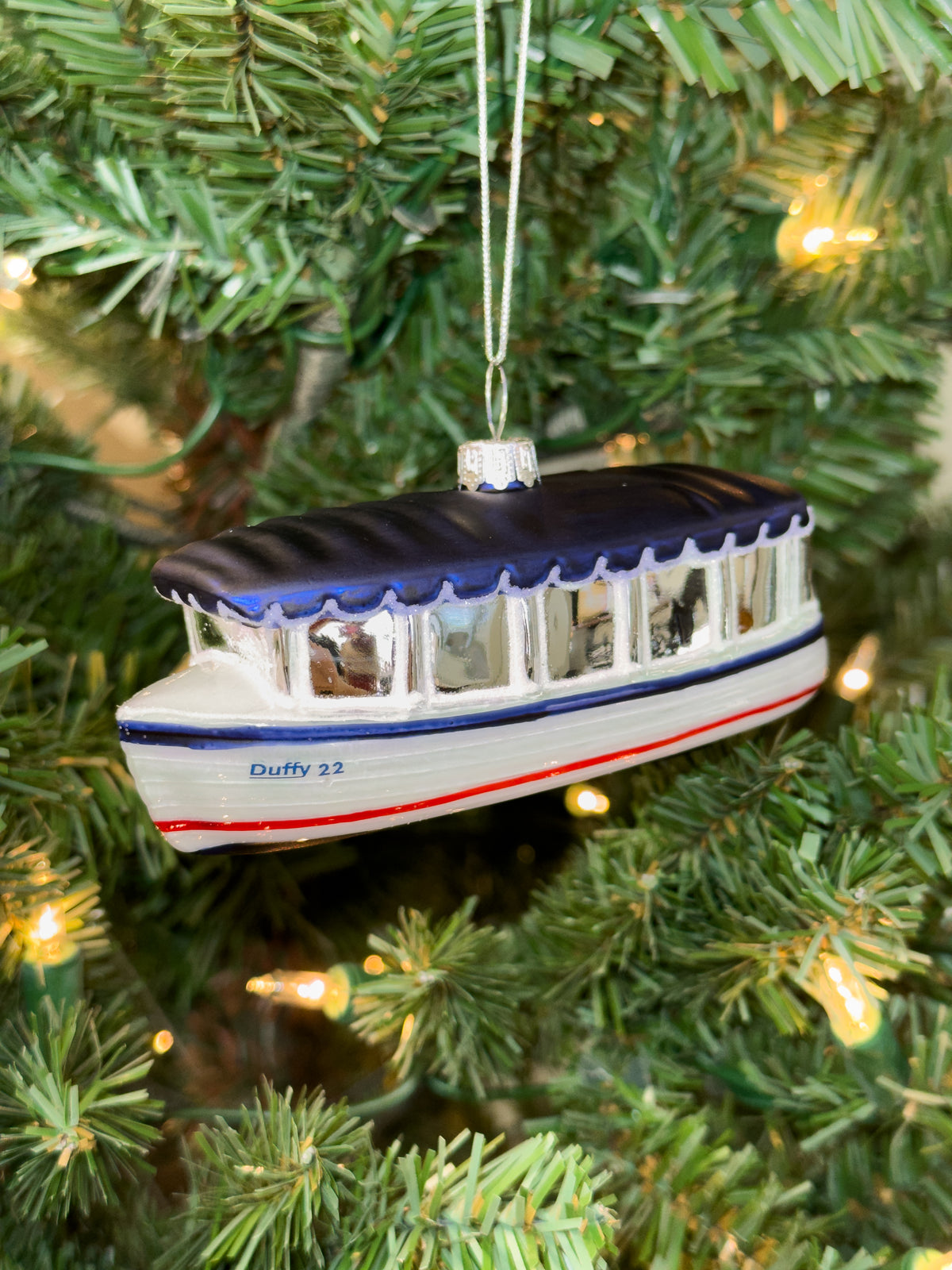 Hand-blown glass ornament of a white Balboa Duffy electric boat with a navy canopy, marked “Duffy 22”