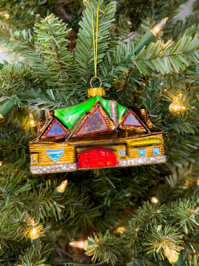 Hand-blown glass ornament of the Laguna Beach Sawdust Festival building with green peaked roofs and a red door